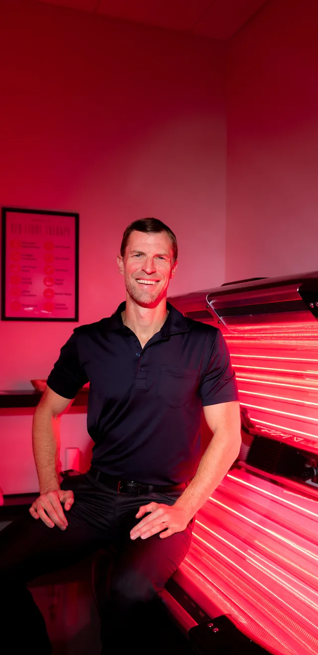 Dr. Josh Axe beside a full-body red light therapy bed at the clinic